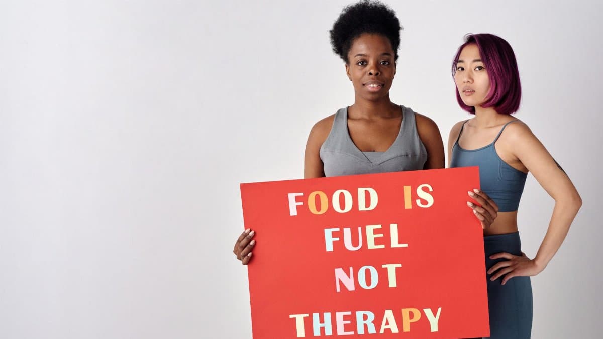 Two women holding a sign saying 'Food is fuel not therapy' promoting a healthy lifestyle.