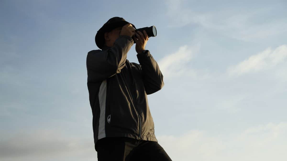 A photographer with a camera in action outdoors beneath a clear blue sky.