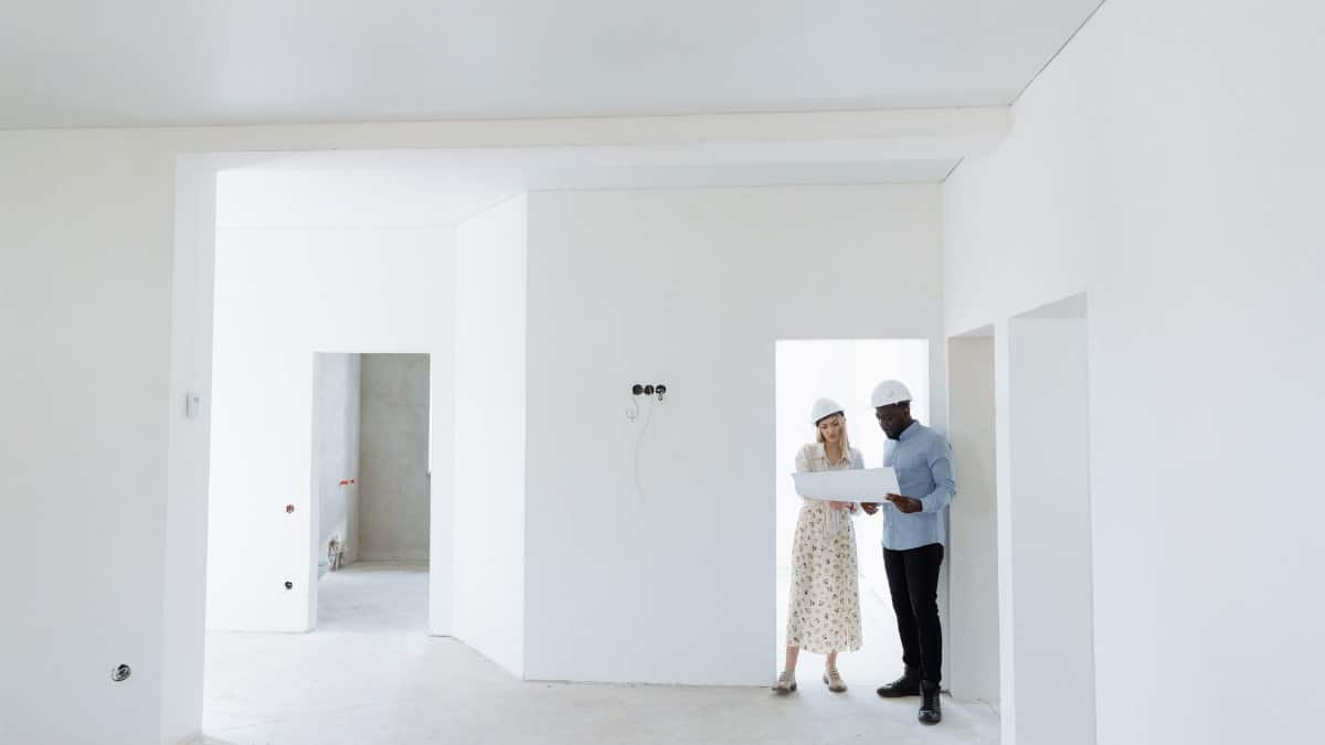 Two architects discuss building plans in a bright, unfinished room.