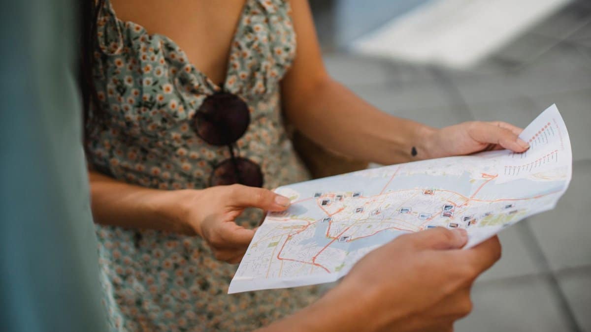 Crop anonymous couple travelers in summer clothes checking location in paper map while walking in unknown city