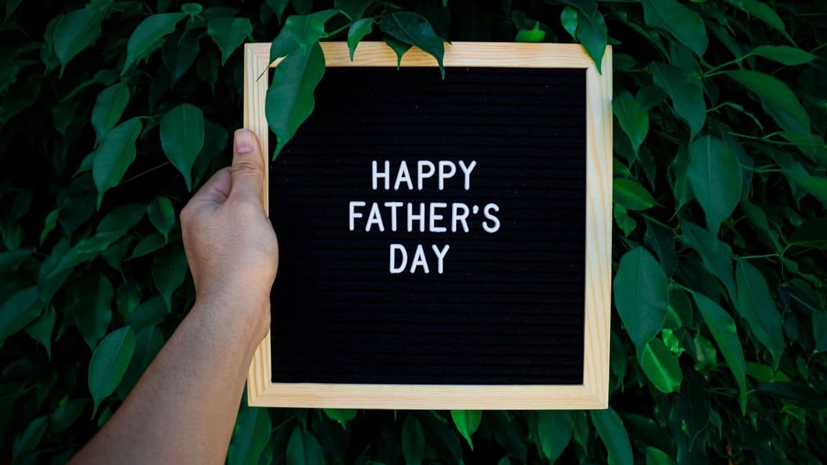 Wooden frame sign with 'Happy Father's Day' text held in front of vibrant green leaves.