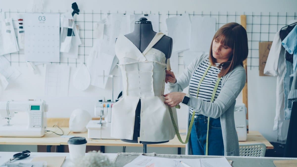 Female fashion designer measuring a dress form in a creative studio workspace.