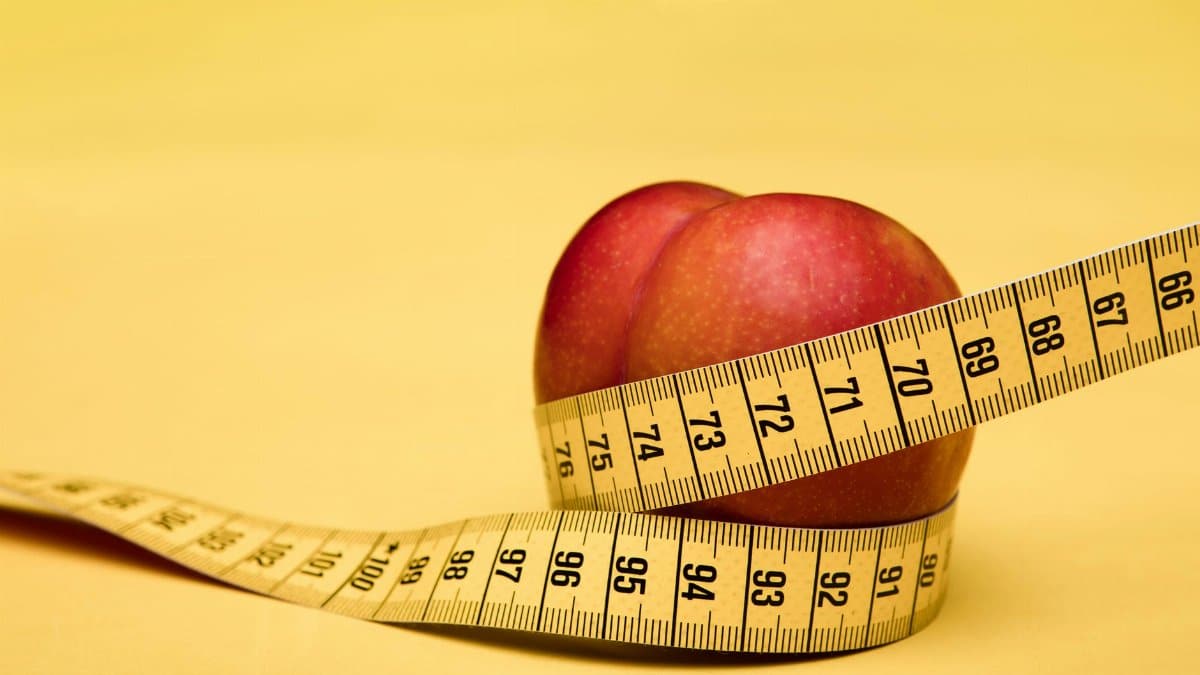 A peach wrapped with a measuring tape on a vibrant yellow background, symbolizing health and measurement.