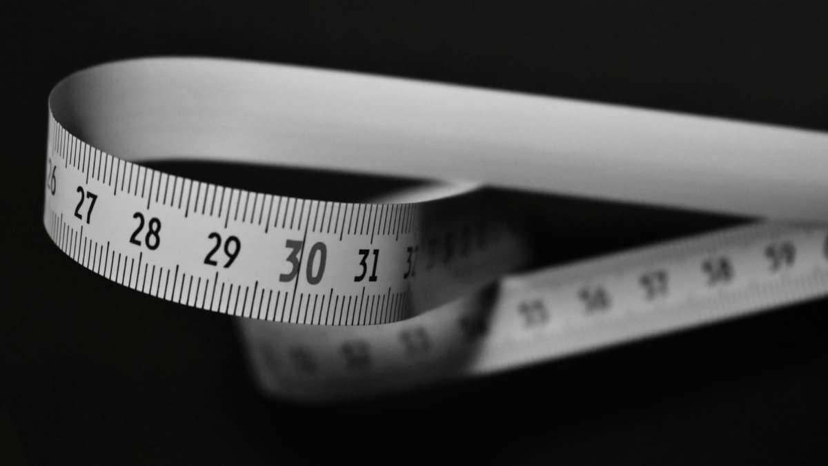 Black and white image of a flexible measuring tape curling on a dark background.