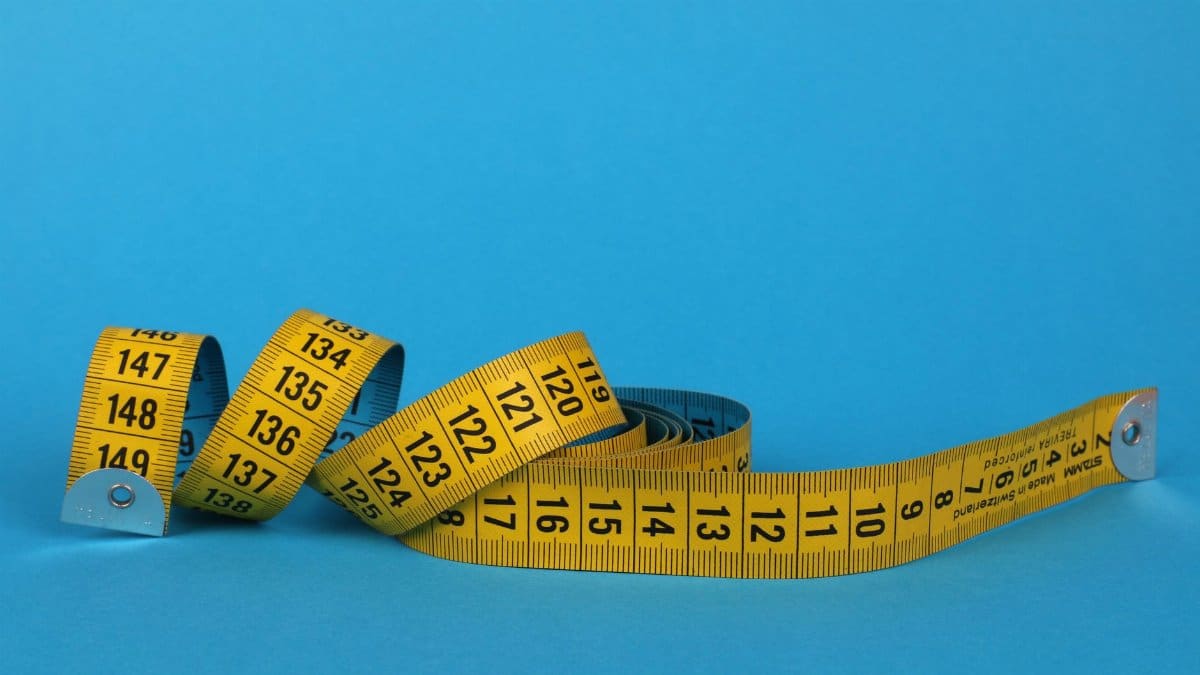Coiled yellow measuring tape against a vibrant blue background, offering ample copy space.