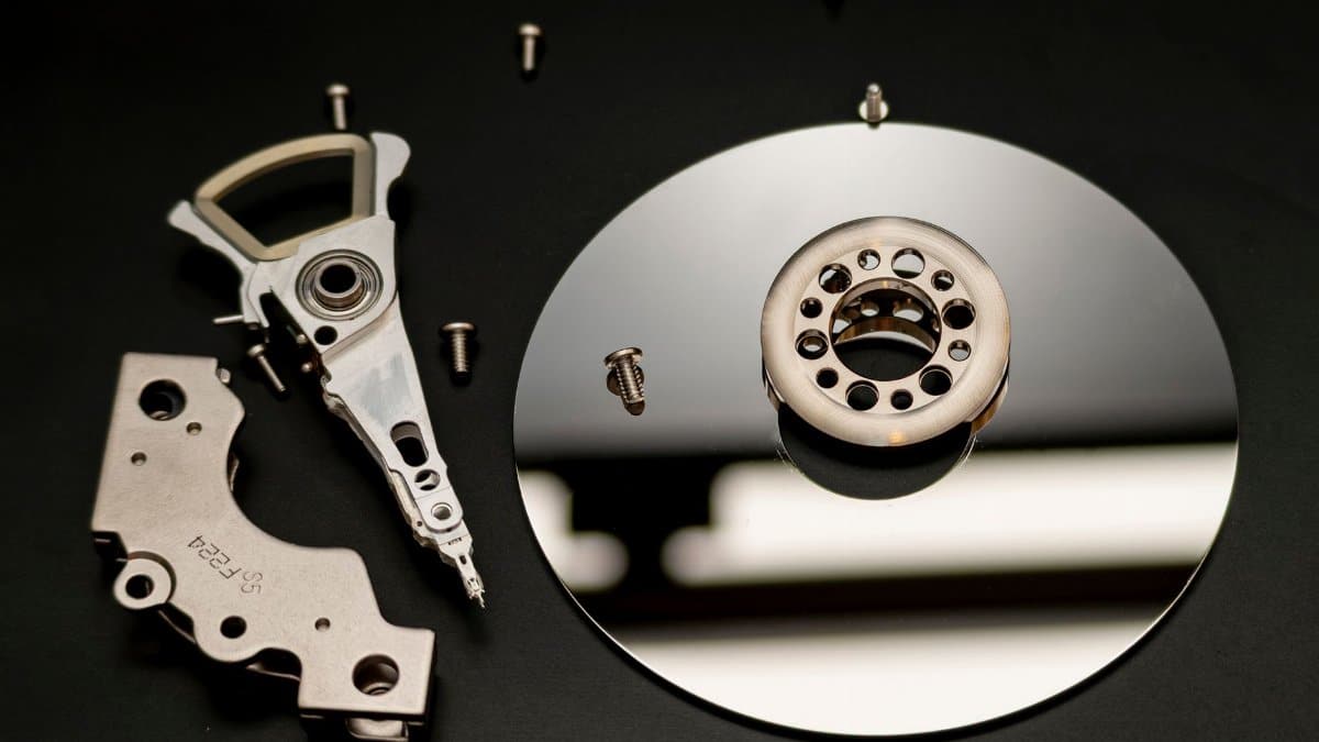 Close-up of dismantled hard drive parts with a reflection on a black surface, showcasing intricate mechanical details.