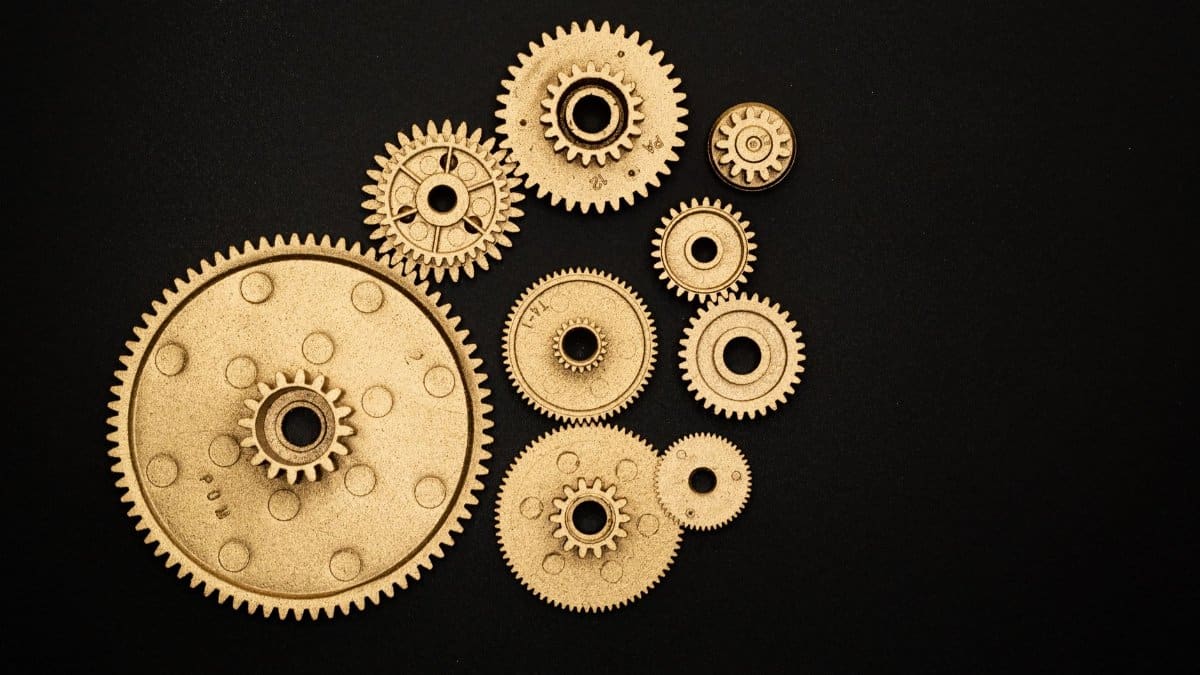 Close-up of golden gears and cogs arranged on a black background, representing teamwork and industry.