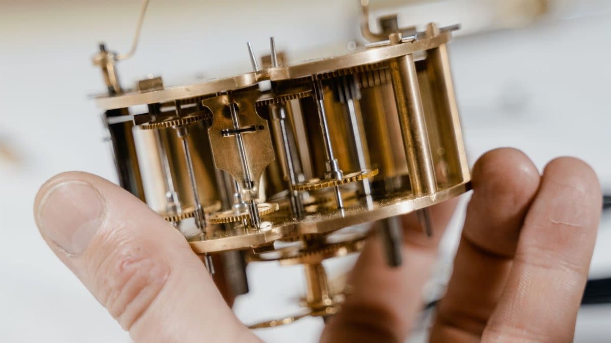 Close-up of a vintage clock mechanism held by hands, showcasing intricate details.