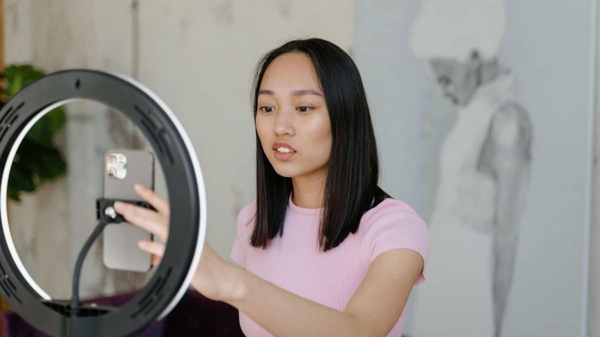 Young woman using a smartphone and ring light for social media content indoors.