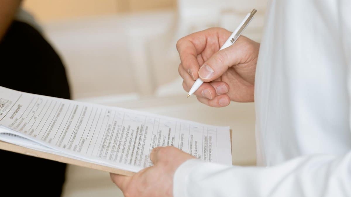 A medical professional in a white coat examines a clipboard with patient documents.