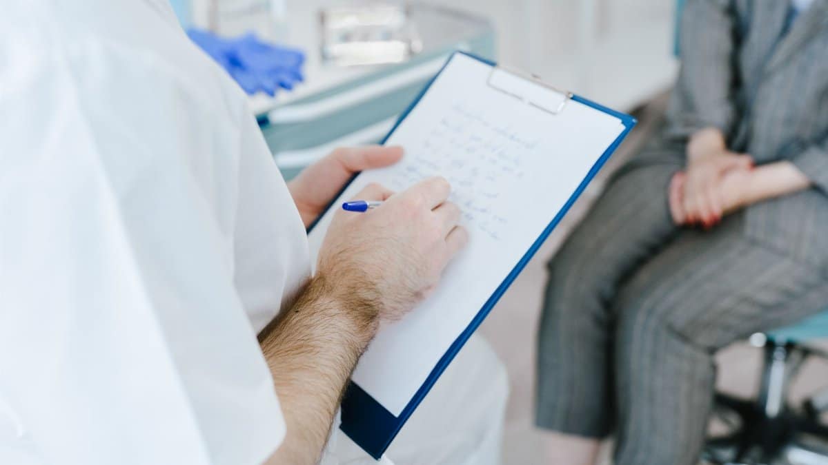 Medical professional writing patient notes on clipboard during consultation.
