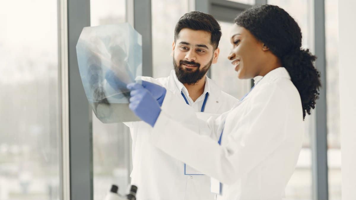 Two doctors in lab coats examine an X-ray image in a bright medical facility.