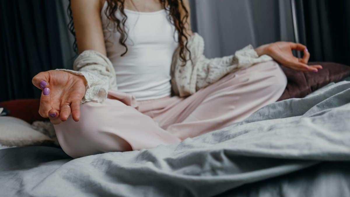A woman practicing yoga meditation on her bed, promoting a peaceful and healthy lifestyle.