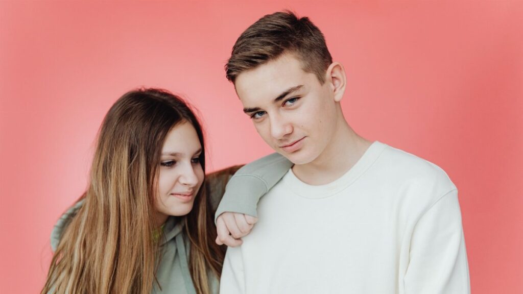 Portrait of a smiling teenage brother and sister against a vibrant pink background, showcasing their youthful energy.