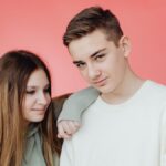 Portrait of a smiling teenage brother and sister against a vibrant pink background, showcasing their youthful energy.