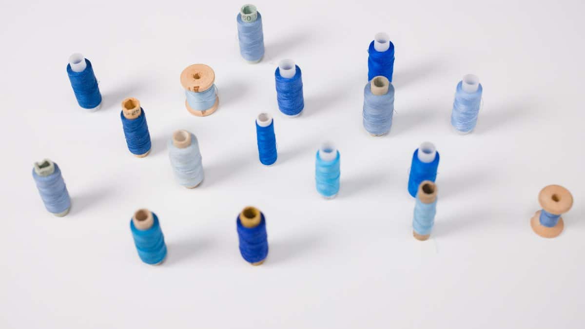 A collection of various blue sewing thread spools arranged on a white surface.