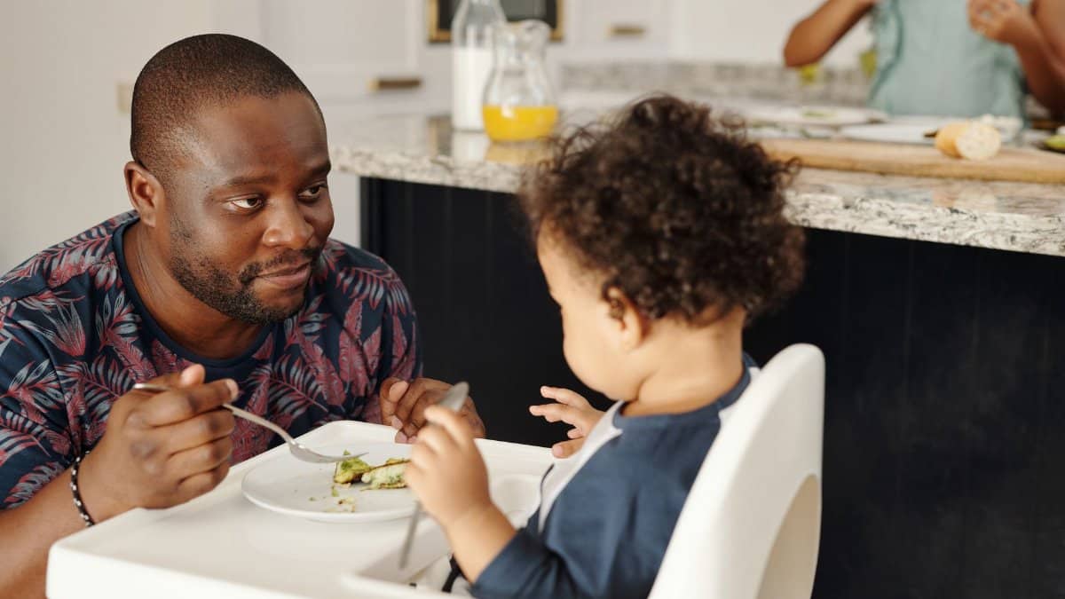 A father shares a meal with his young child in the kitchen, capturing a tender family moment.
