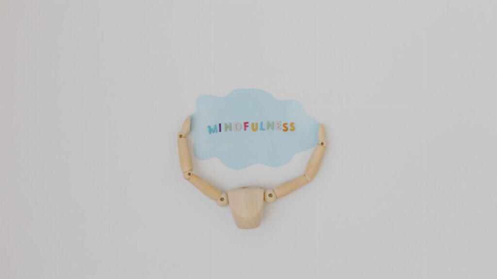 Minimalist image of a wooden figure holding a speech bubble saying 'Mindfulness'.