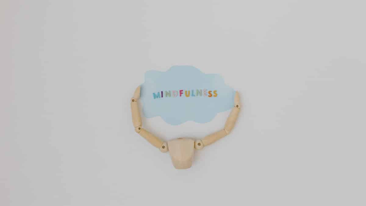Minimalist image of a wooden figure holding a speech bubble saying 'Mindfulness'.