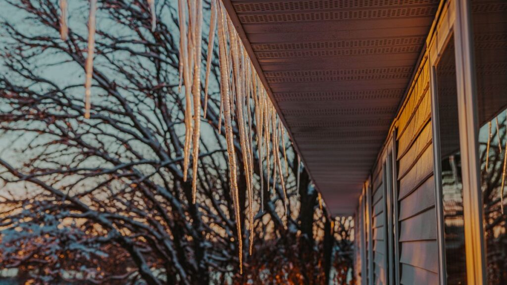 Long icicles hang from a roof at sunset during a Minnesota winter, casting warm hues.