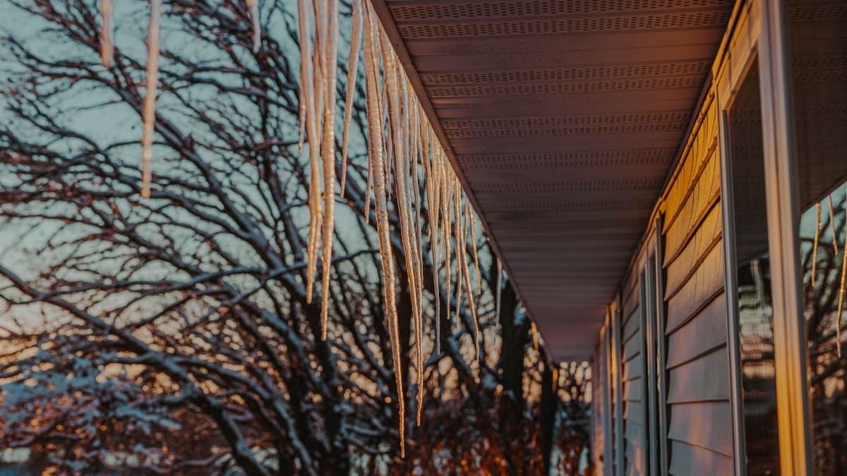 Long icicles hang from a roof at sunset during a Minnesota winter, casting warm hues.