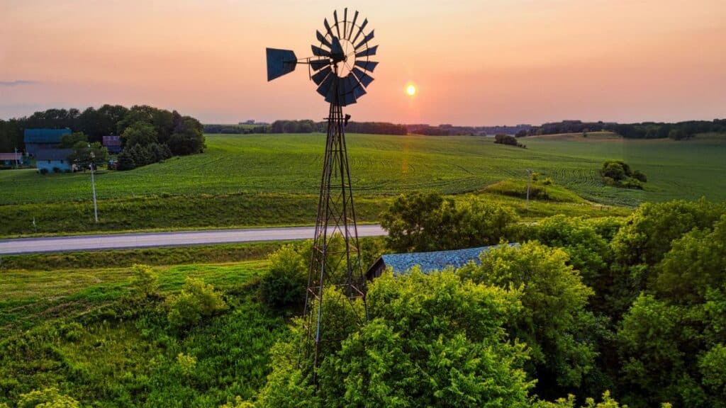 Scenic view of a windmill and lush farmland at sunset in rural Minnesota, USA.