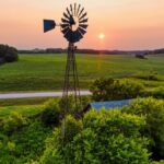 Scenic view of a windmill and lush farmland at sunset in rural Minnesota, USA.
