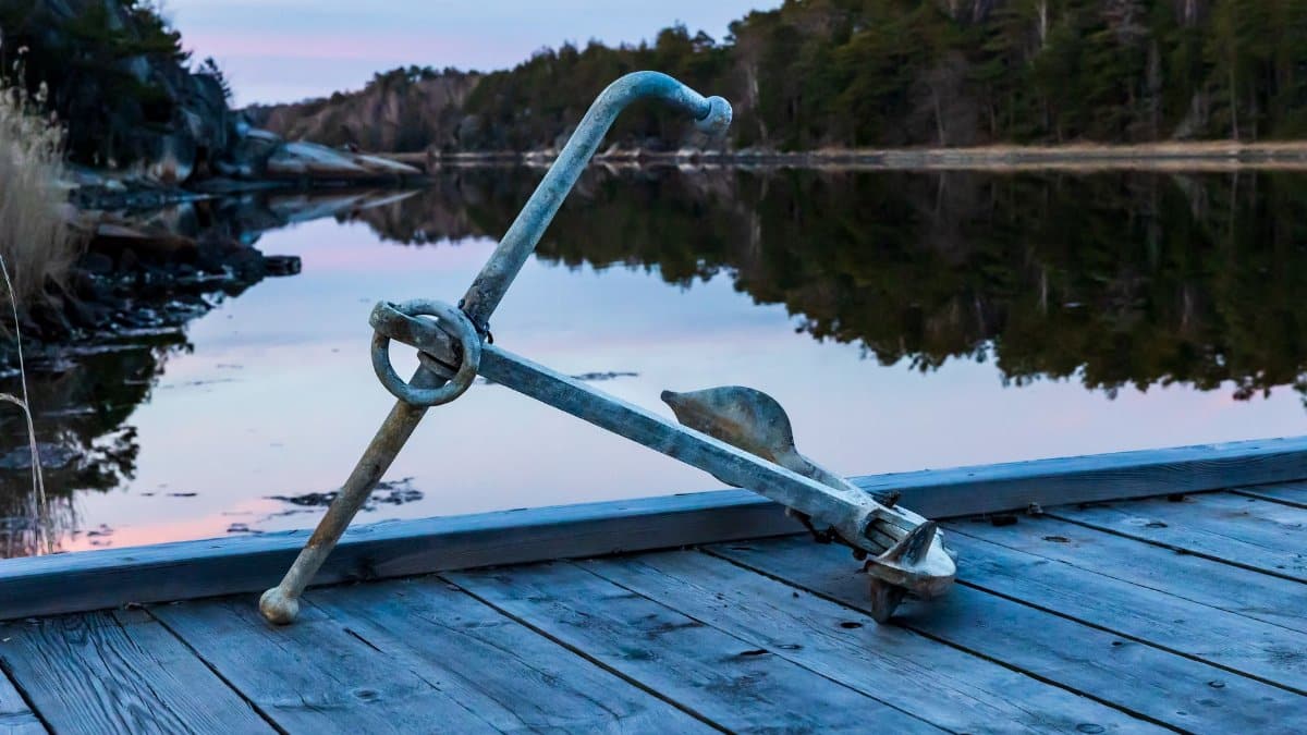 An old anchor rests on a pier by a tranquil lake in Raftötången during sunset, reflecting serene nature.