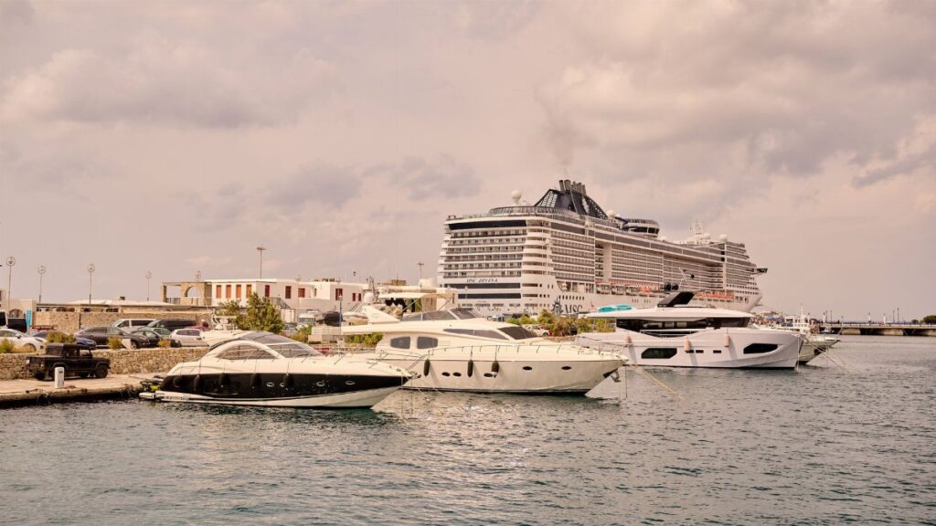 A scenic view of luxury yachts and a cruise ship moored at a bustling port under cloudy skies.