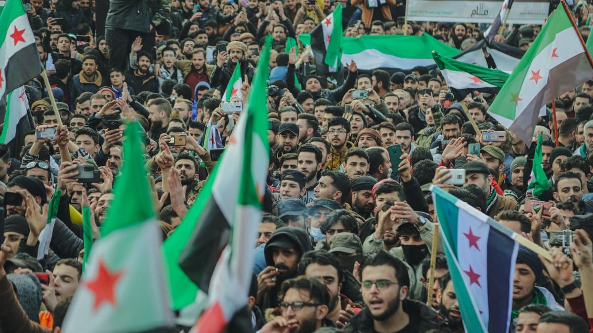 Large crowd in Syria waving flags during a protest, demonstrating unity and political expression.
