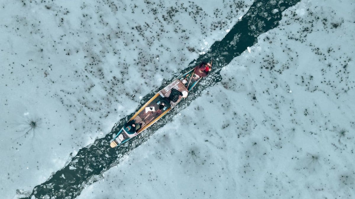 An aerial shot capturing a kayak navigating a frozen river, highlighting winter's icy beauty.