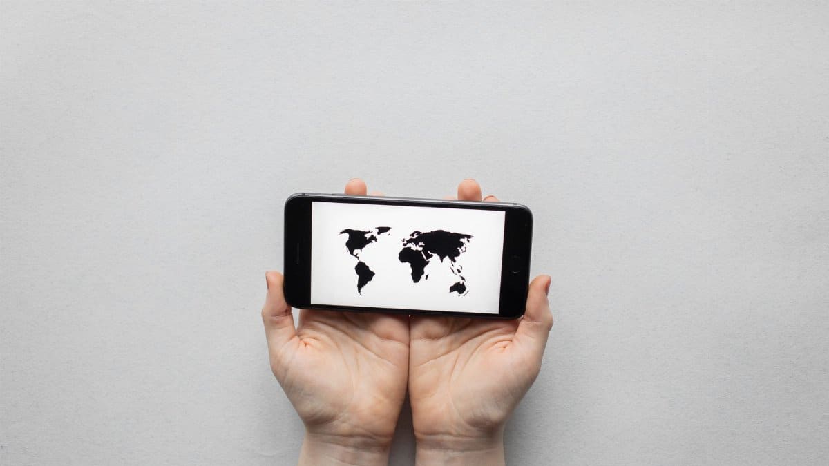 Hands holding a smartphone displaying a world map on a white background.