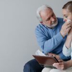 A senior couple embracing and wiping away tears while reminiscing with a photo album.