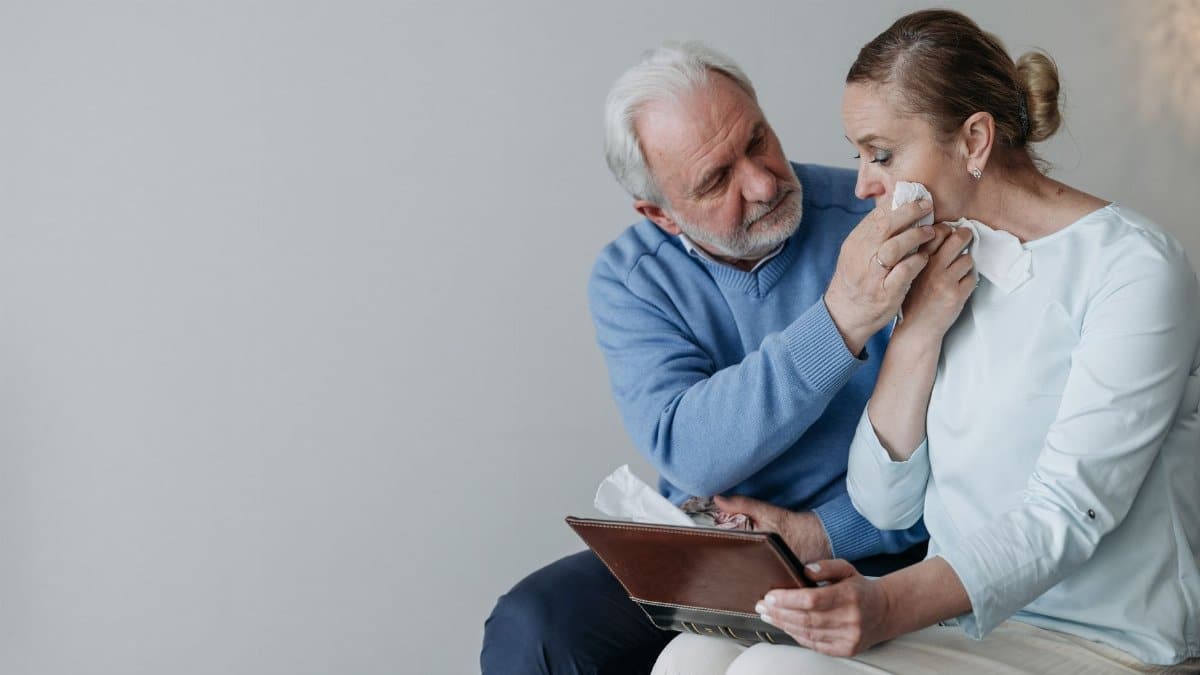 A senior couple embracing and wiping away tears while reminiscing with a photo album.