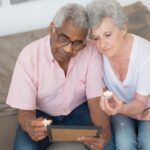 An elderly couple sits on a sofa with a picture frame, reflecting with candles.