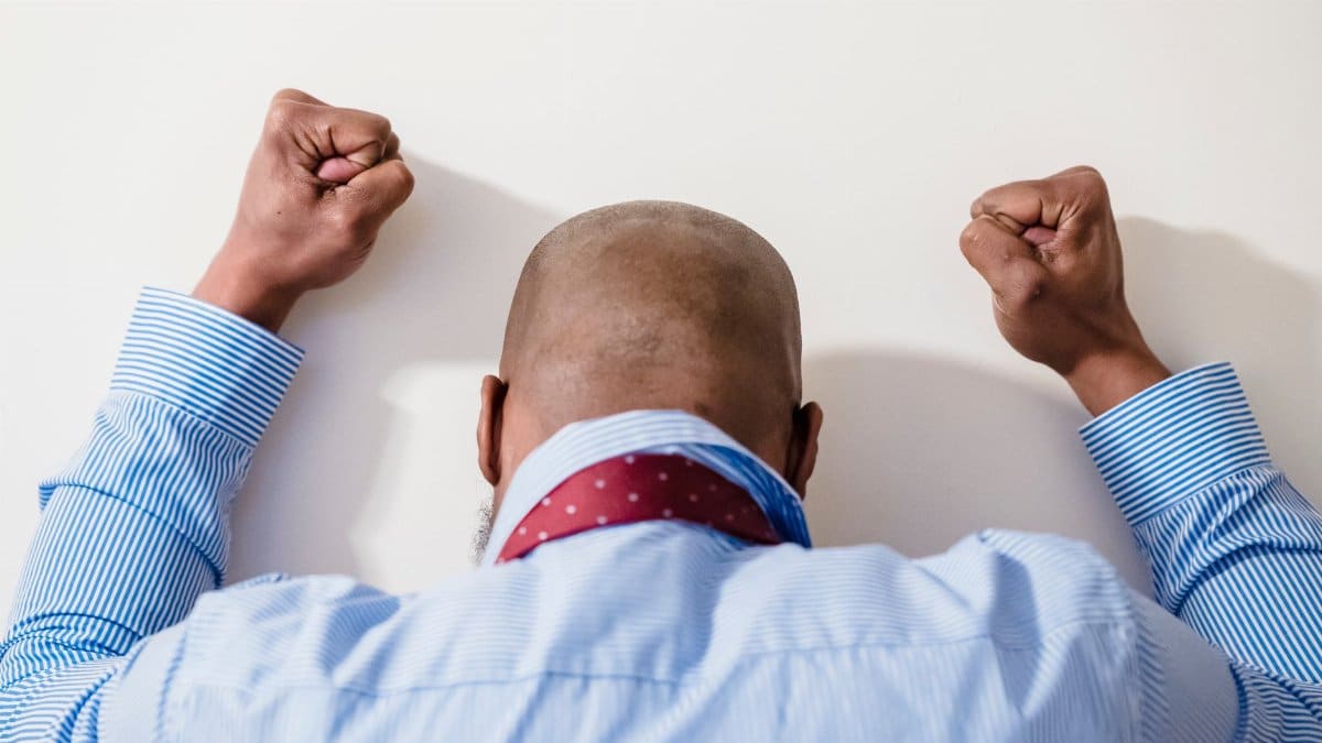 A bald man in a blue striped shirt with clenched fists expressing frustration against a white background.