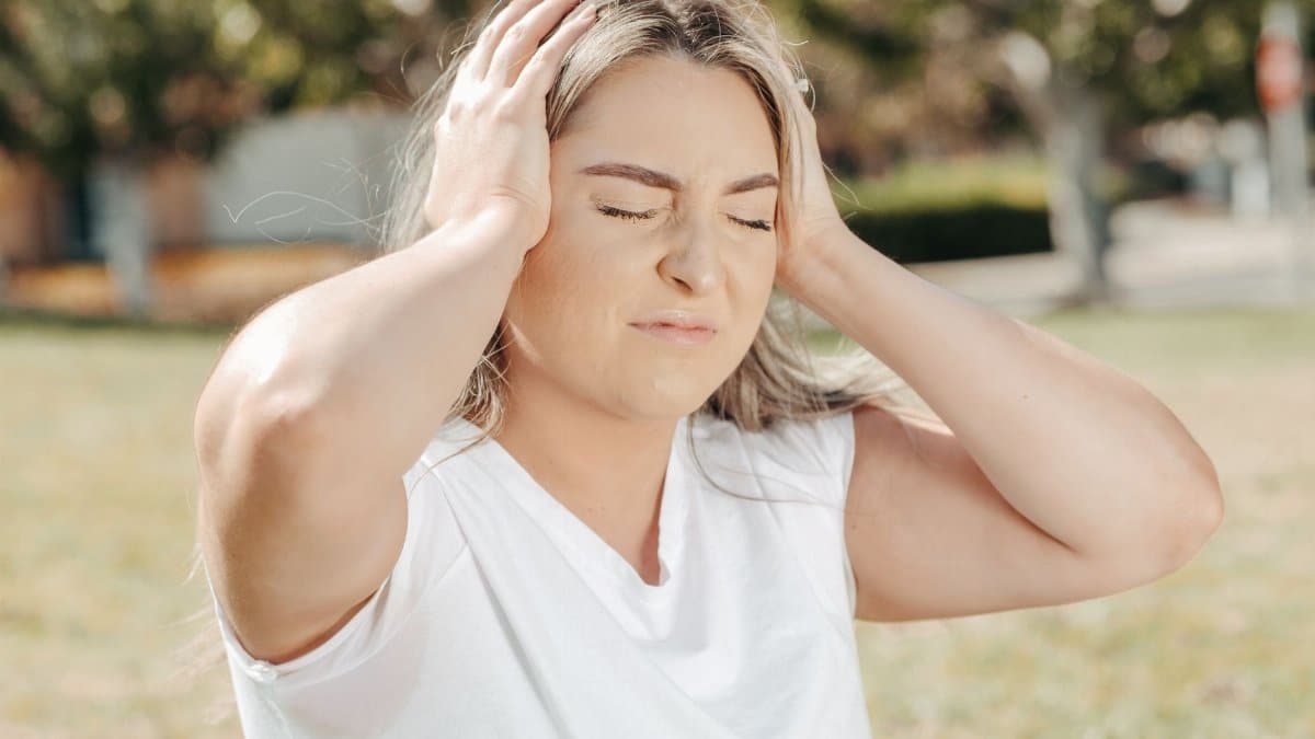 A woman outdoors holds her head, depicting stress or a headache.