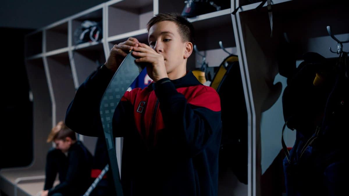 Teen boy taping hockey stick in locker room before a game, capturing the focus and determination of young athletes.