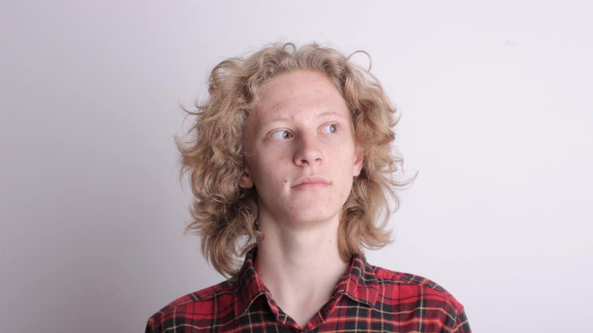 A pensive young man with blonde hair in a plaid shirt, looking away thoughtfully.
