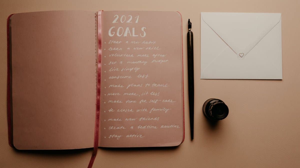 Open notebook with 2021 goals, calligraphy pen, envelope, and ink jar on neutral background.