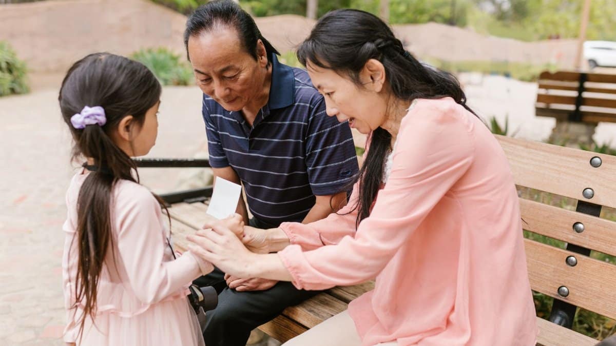 Asian family bonding outdoors, with adults sitting on a bench engaging with a child.