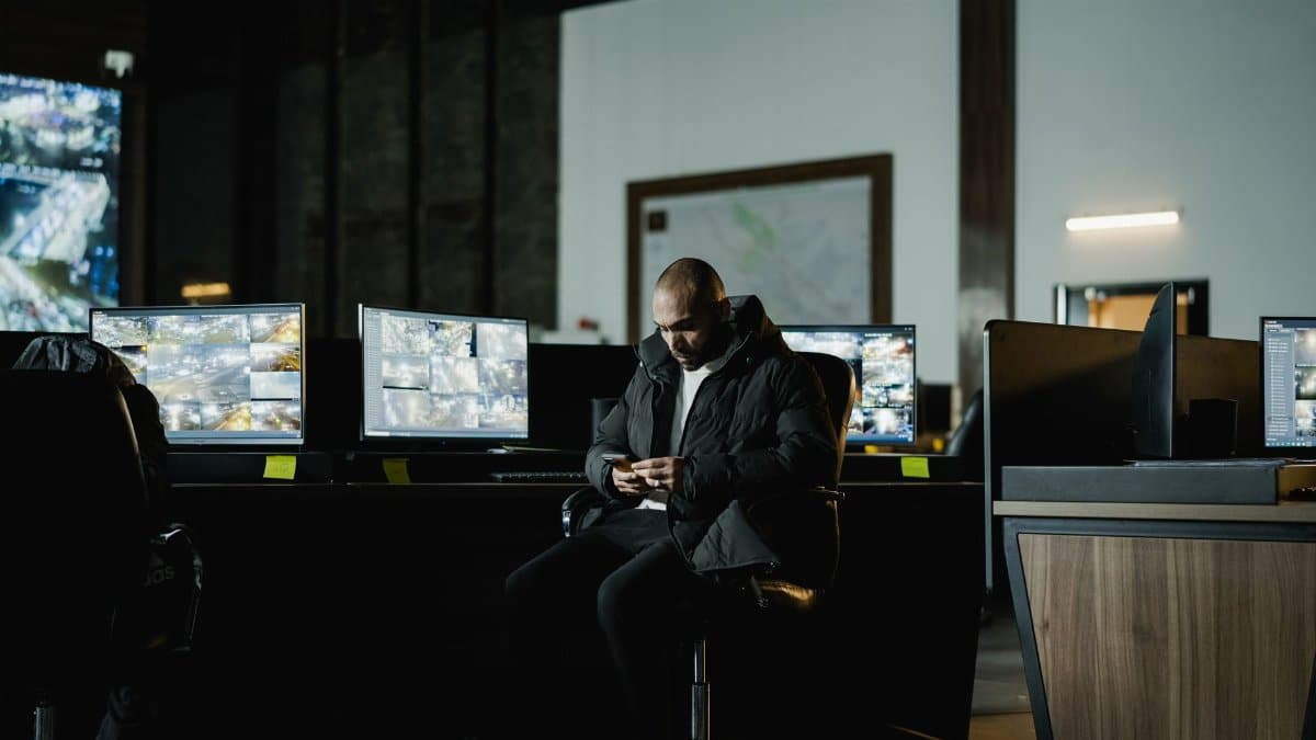 Security officer seated in a dimly lit control room, analyzing multiple surveillance screens.