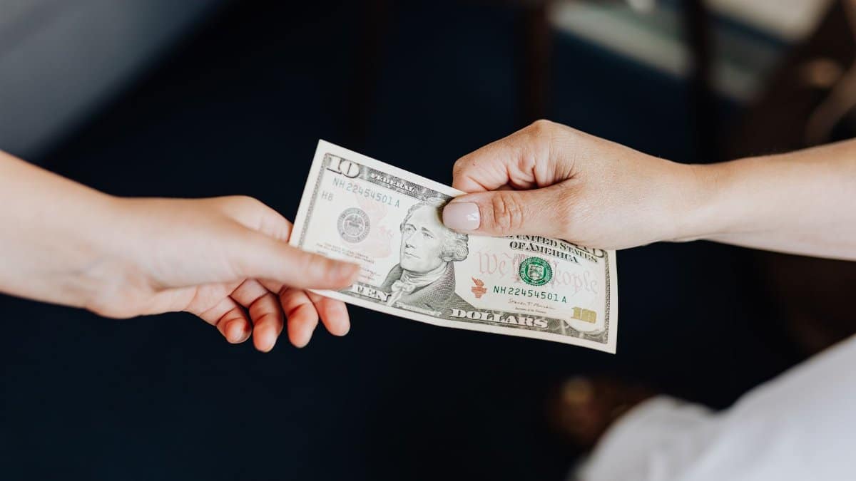 Two people exchanging a ten dollar bill in a close-up hand-to-hand transaction.