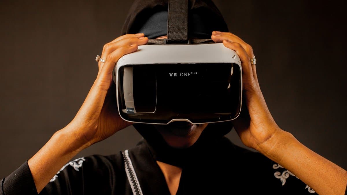A woman wearing a black headscarf enjoys a virtual reality experience indoors.