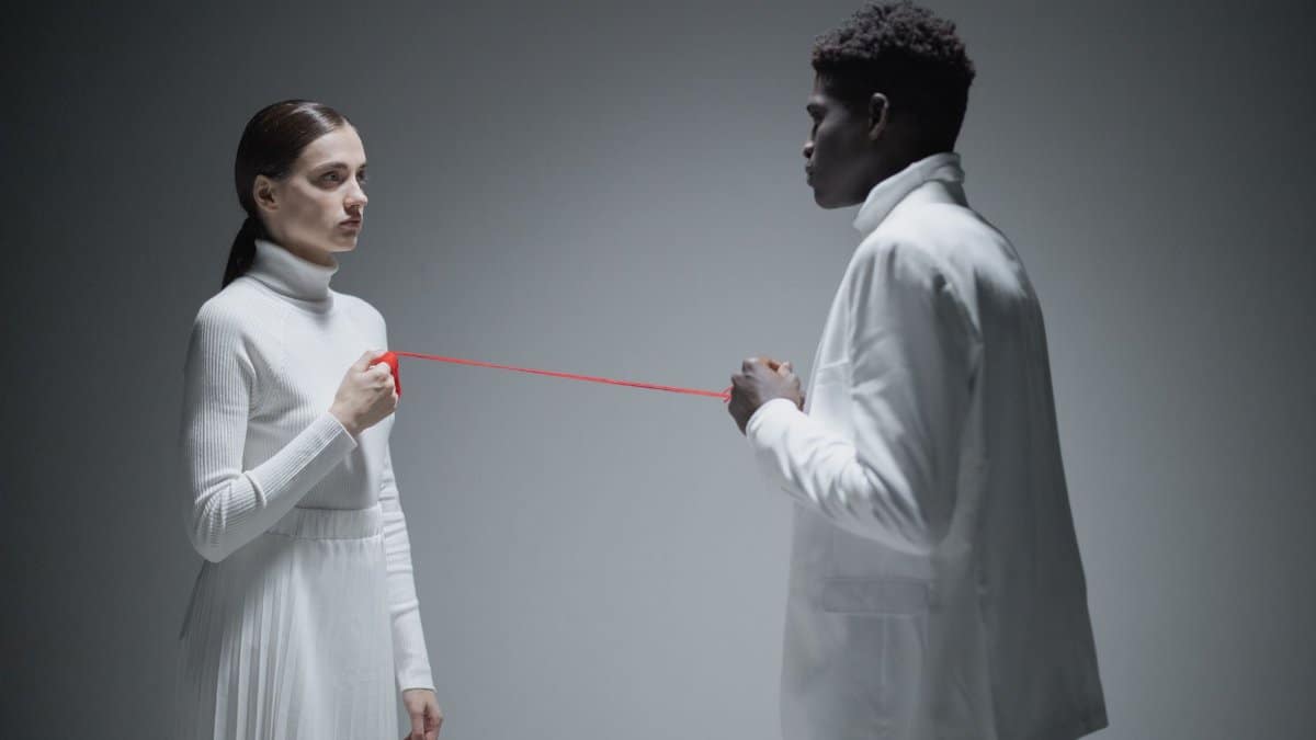 Multiracial couple holding red string symbolizing connection in studio.