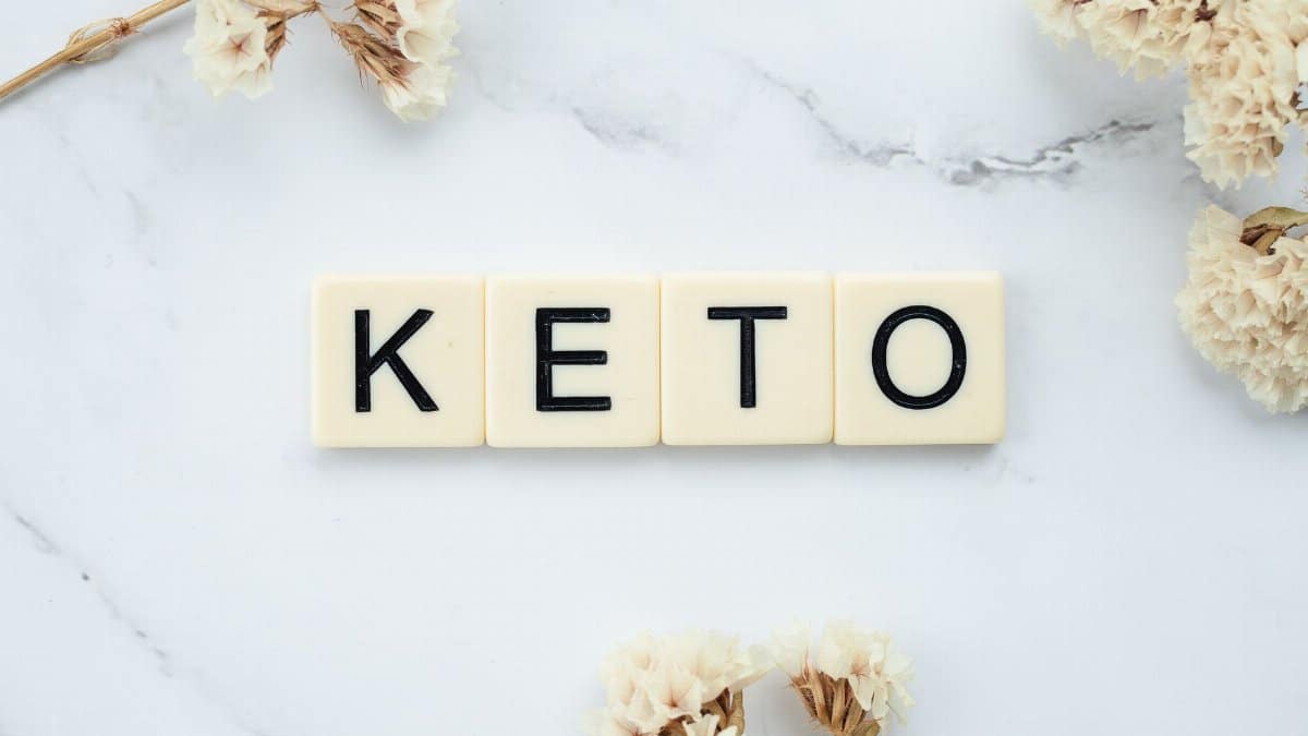 Scrabble tiles spelling 'Keto' on a marble surface with white flowers, symbolizing a ketogenic lifestyle.