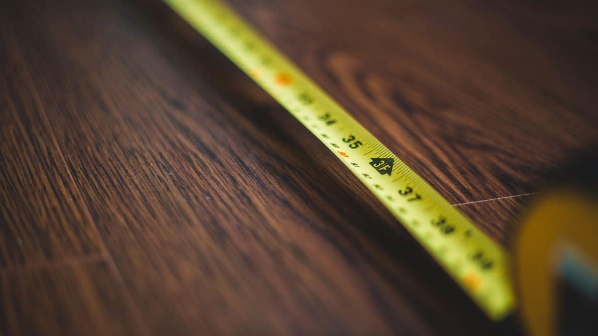 Yellow tape measure extended across a dark wooden floor, highlighting measurement details.