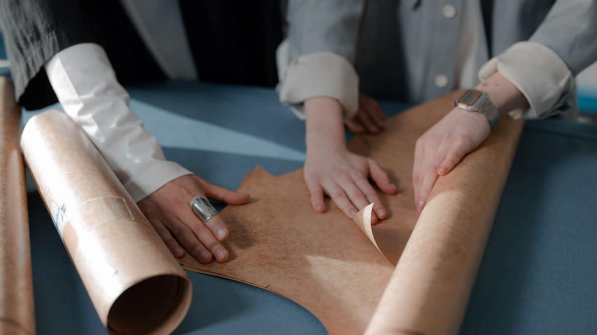 Close-up of hands working on paper patterns for dressmaking in an indoor workshop setting.