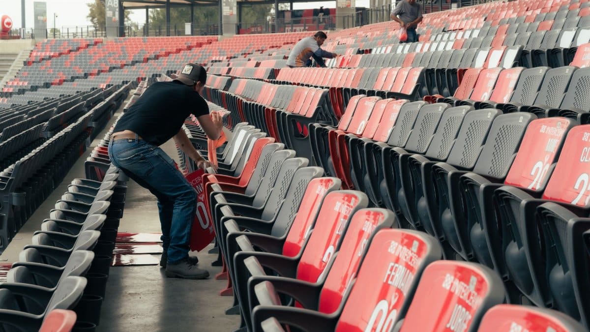 Event staff organizing stadium seating for an upcoming sports event with empty grandstands.
