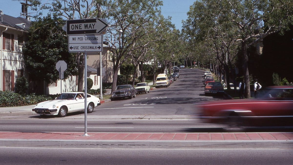 A busy urban street featuring cars, one way signs, and lush green trees.